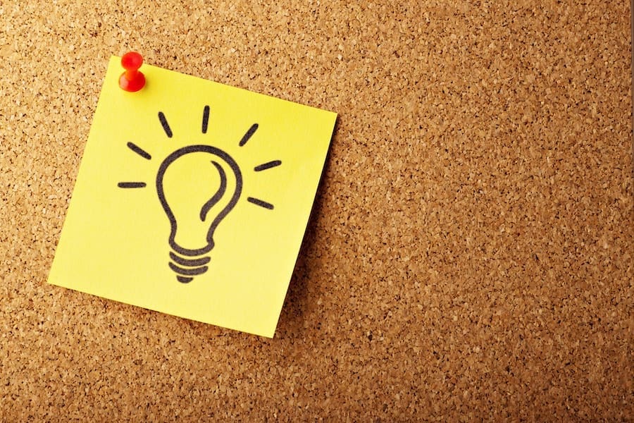 A sticky note with a lightbulb drawn on it pinned to a cork board