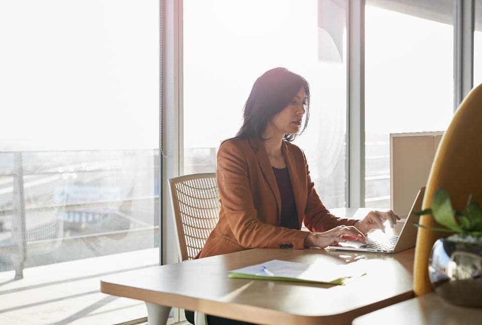 A woman, new business owner, typing on a computer in a high rise office setting